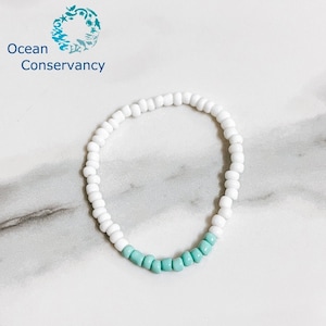 May include: White and light blue beaded bracelet. The bracelet is made of small, round beads. The beads are white for most of the bracelet, with a band of light blue beads at the bottom.