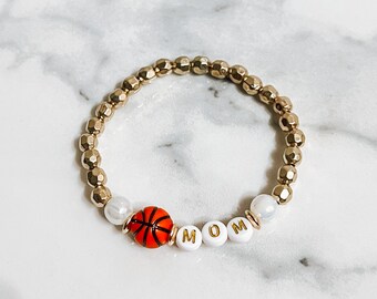 May include: Gold beaded bracelet with a basketball charm and white beads spelling "MOM".