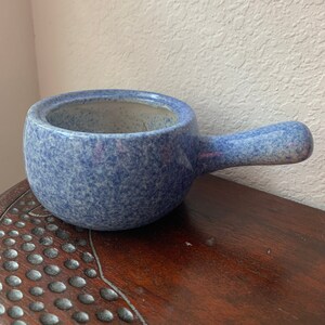 May include: A blue speckled ceramic pot with a handle. The pot is round and has a speckled blue glaze.