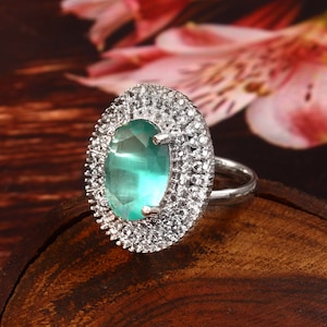 Puede incluir: Un anillo de plata con una gran piedra preciosa ovalada verde rodeada de pequeñas piedras preciosas transparentes.