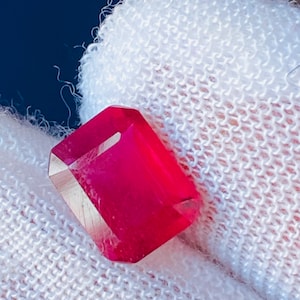 Puede incluir: Una piedra preciosa de color rojo intenso con un corte rectangular, expuesta sobre un fondo de tela blanca.