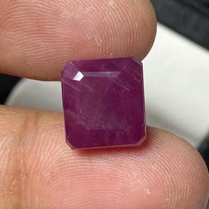 May include: A deep pink emerald cut gemstone with facets.