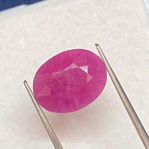 Może przedstawiać: Owalny, różowy kamień szlachetny z fasetkami, trzymany przez pęsetę na białym tle.