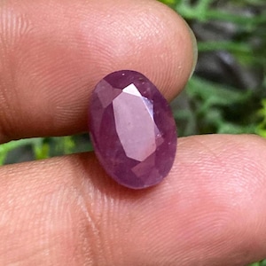 May include: A deep pink oval-shaped gemstone with a faceted cut.
