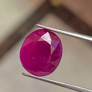 May include: A deep red oval-shaped gemstone with a faceted cut.