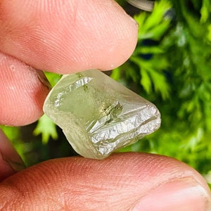 Peut inclure: Un cristal vert clair avec une surface brute et facetée. Le cristal est translucide et a une légère teinte jaune.