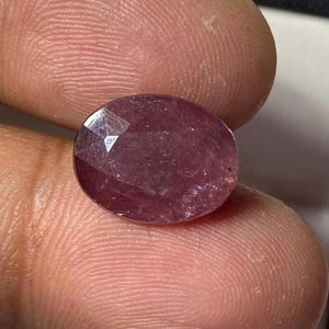 Könnte beinhalten: Ein ovaler Edelstein in tiefem Rosa mit facettiertem Schliff.