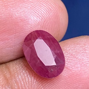 Puede incluir: Una gema ovalada de color rosa vibrante con un corte facetado. La gema está colocada sobre un fondo rosa.