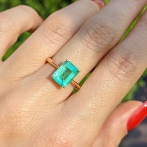 Puede incluir: Un anillo de oro con una gran piedra preciosa verde esmeralda. La piedra preciosa está tallada en forma de esmeralda.