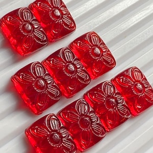 Op de afbeelding: Vijf rode glazen tegels met een bloemmotief. De tegels zijn vierkant en hebben een reliëfbloemmotief.