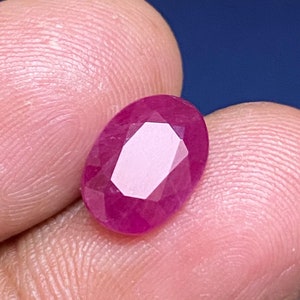 Puede incluir: Una piedra preciosa de rubí ovalada de color rosa vibrante con un corte facetado.
