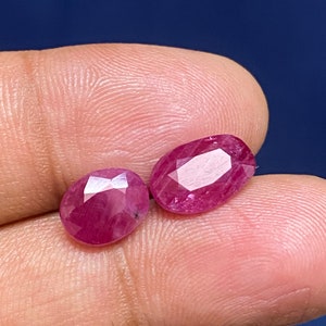 Puede incluir: Dos piedras preciosas de rubí de forma ovalada y facetadas. Los rubíes son de color rosa intenso y tienen un alto pulido.