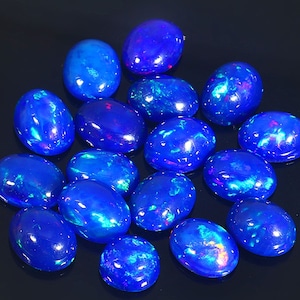 Op de afbeelding: Een verzameling ovale blauwe opalen met iriserende kleurvlekken. De opalen zijn in een cluster op een zwarte achtergrond gerangschikt.
