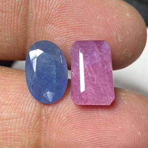 May include: Two oval-shaped gemstones, one blue and one pink, are displayed on a finger.
