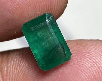 May include: A vibrant green emerald gemstone with a rectangular cut and a polished finish.