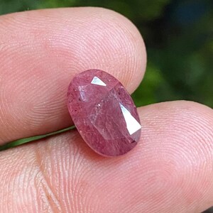 Puede incluir: Una piedra preciosa ovalada de color rosa con un corte facetado. La piedra preciosa tiene una apariencia translúcida con un ligero brillo.