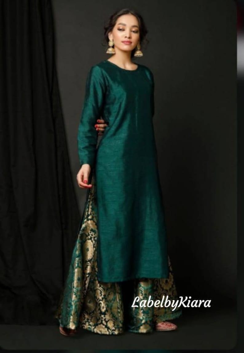 Op de afbeelding: Een tealgroene, langarmige kurta met een ronde halslijn, gecombineerd met gouden en groene brokaat palazzo-broeken. De outfit is gestyled met gouden oorbellen en de tekst "LabelbyKiara" is zichtbaar onderaan de afbeelding.