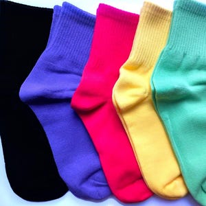 May include: A set of five ankle socks arranged in a row, featuring solid colours including black, purple, hot pink, yellow, and light green. Each sock has a ribbed cuff at the top and a smooth knit texture throughout the foot and heel area.