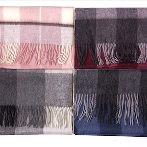 May include: Four folded scarves arranged in a square. Each scarf has a plaid design and fringing. The colours are pink, grey, black, and blue. The scarves appear to be made of a soft material.