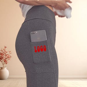 May include: Gray leggings with a large pocket on the left thigh. The pocket has a black smartphone inside and the word "LOGO" printed in red.