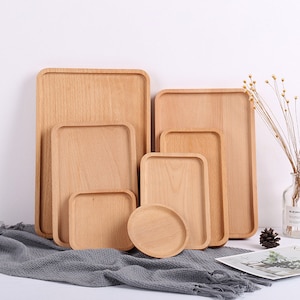 May include: Set of five wooden trays in various sizes, ranging from small to large. The trays are all rectangular and have a natural wood finish. They are arranged in a staggered pattern, with the largest tray at the back and the smallest tray at the front.