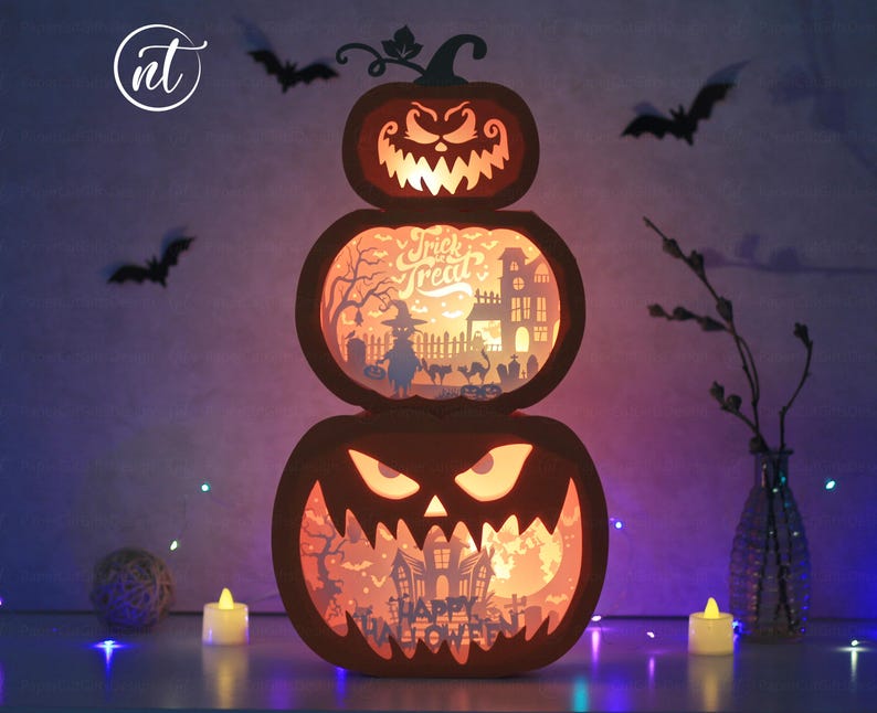 Może przedstawiać: Trzypoziomowa dekoracja z dyni na Halloween z wyrzeźbionymi twarzami i scenami wewnętrznymi. G&oacute;rna dynia ma wyrzeźbioną twarz, środkowa m&oacute;wi "Trick or Treat", a dolna "Happy Halloween". Nietoperze i świece otaczają dekorację.