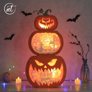 May include: A three-tiered orange pumpkin decoration with carved faces and interior scenes, including a haunted house and the words "Trick or Treat" and "Happy Halloween". Black bat silhouettes and candles complete the Halloween theme.