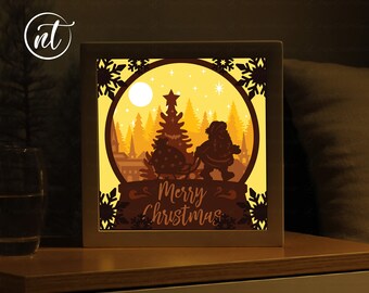 Puede incluir: Un globo de nieve iluminado de papel recortado con una silueta de Papá Noel tirando de un trineo con un árbol de Navidad dentro. El globo de nieve está iluminado con luz amarilla cálida y el texto "Merry Christmas" está escrito debajo del globo de nieve.