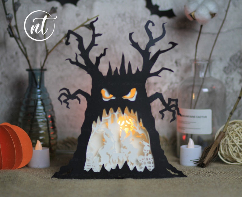 Op de afbeelding: Een zwarte papieren Halloween-decoratie in de vorm van een boom met een griezelig gezicht. De boom heeft een witte binnenkant met een gloeiend licht erin.
