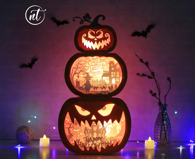 Może przedstawiać: Trzypoziomowa dekoracja z dyni na Halloween z wyrzeźbionymi twarzami i scenami wewnętrznymi. G&oacute;rna dynia ma łodygę i groźny uśmiech. Środkowa dynia m&oacute;wi "Trick or Treat" i pokazuje upiorne miasto. Dolna dynia m&oacute;wi "Happy Halloween".