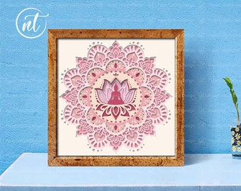 May include: A framed print of a pink and white mandala with a meditating figure in the center. The mandala is intricate and detailed, with a layered design.