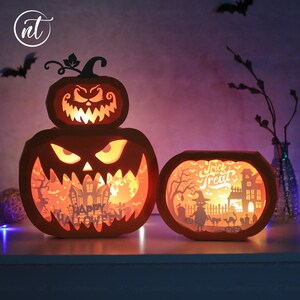 Może przedstawiać: Pomarańczowe lampiony z dyni wycięte z papieru o tematyce Halloween z podświetlanymi wnętrzami. Większy lampion ma warstwowy wz&oacute;r z wyrzeźbioną twarzą i napisem "Happy Halloween". Mniejszy lampion m&oacute;wi "Trick or Treat". Nietoperze w tle.
