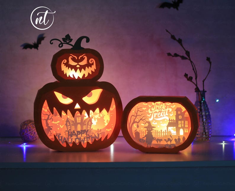 Może przedstawiać: Pomarańczowe lampiony z dyni wycięte z papieru o tematyce Halloween z podświetlanymi wnętrzami. Większy lampion ma warstwowy wz&oacute;r z wyrzeźbioną twarzą i napisem "Happy Halloween". Mniejszy lampion m&oacute;wi "Trick or Treat". Nietoperze w tle.