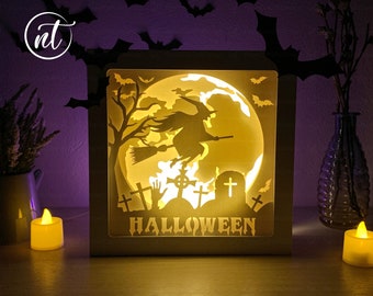 May include: A white wooden box with a Halloween scene inside. The scene features a witch flying on a broomstick in front of a full moon. The words "HALLOWEEN" are printed below the moon.