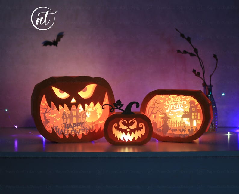 Może przedstawiać: Trzy podświetlane pomarańczowe papierowe dynie z wyrzeźbionymi twarzami i scenami Halloween. Największa dynia ma napis "Happy Halloween". Środkowa dynia jest mniejsza, a prawa dynia ma napis "Trick or Treat". Nad nimi leci sylwetka nietoperza.