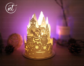 Könnte beinhalten: Ein weißer Papier-Kerzenhalter mit einem ausgeschnittenen Design von Weihnachtsmann, der mit einem Sack voller Geschenke einen Schornstein hochklettert. Das Design beinhaltet auch ein Haus und Bäume. Der Kerzenhalter ist angezündet und strahlt ein warmes Licht aus.