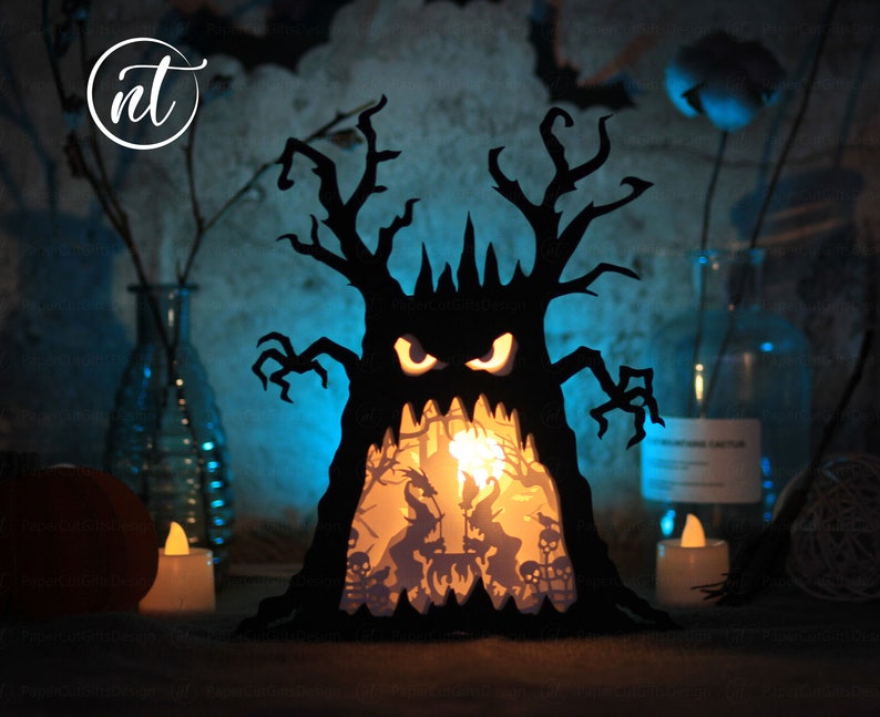 Op de afbeelding: Een zwarte papieren Halloween-boom met een griezelig gezicht en een gloeiend interieur. De boom wordt van binnenuit verlicht, waardoor een griezelige en feestelijke sfeer ontstaat.