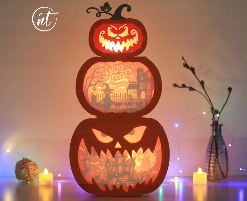 Może przedstawiać: Trzypoziomowa dekoracja na Halloween w kształcie dyni. G&oacute;rna dynia ma wyrzeźbioną twarz z groźnym wyrazem. Środkowa dynia ma napis "Trick or Treat" i upiorną scenę. Dolna dynia ma wyrzeźbioną twarz.