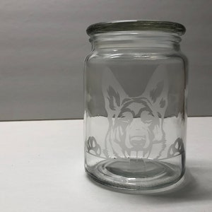 Pode incluir: Um frasco de vidro transparente com tampa, apresentando um design gravado da cabe&ccedil;a de um c&atilde;o pastor alem&atilde;o olhando por cima.