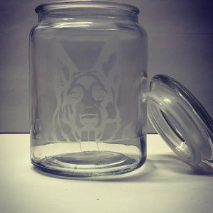 Pode incluir: Um frasco de vidro transparente com tampa, apresentando um design gravado da cabe&ccedil;a de um c&atilde;o pastor alem&atilde;o.