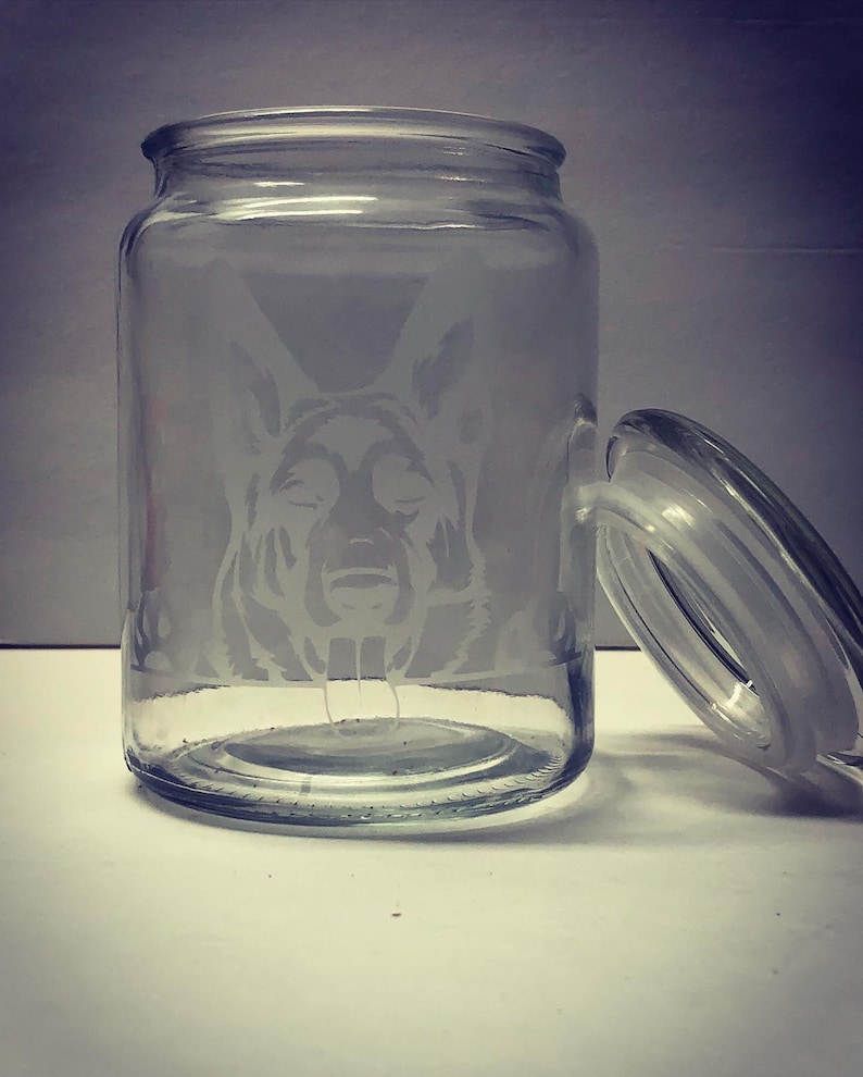 Pode incluir: Um frasco de vidro transparente com tampa, apresentando um design gravado da cabe&ccedil;a de um c&atilde;o pastor alem&atilde;o.