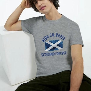 Puede incluir: Camiseta gris con una bandera escocesa azul y blanca y el texto "Alba gu Bràth" y "Scotland Forever".