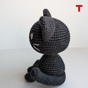 May include: A black crocheted cat toy with white embroidered facial features. The cat is sitting with its tail curled around its body.