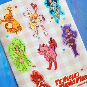 Może przedstawiać: Arkusz naklejek z ilustracjami postaci w stylu anime. Arkusz ma różowo-białe kratkowane tło z sercami. Tekst "Tokyo Mew Mew" jest wyświetlany w kolorze czerwonym i białym.