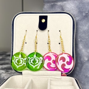 May include: A jewelry box with four pairs of earrings. Two pairs are green with white designs and two pairs are pink with white designs.