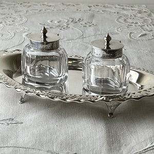 May include: A silver tray with two clear glass jars with silver lids. The tray has a scalloped edge and three feet.