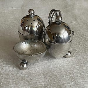 Könnte beinhalten: Ein dreiteiliges Gewürzset aus Silber mit einer runden Schale und zwei eiförmigen Streuern mit Deckeln.