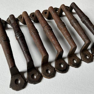 May include: Eight rustic, brown metal drawer pulls with a simple, curved design. The pulls have a worn, aged look, giving them a vintage feel.