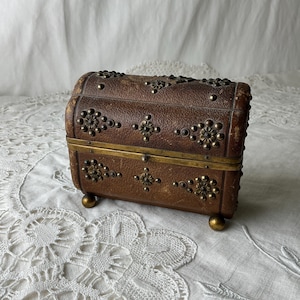 May include: A small, brown wooden box with brass accents and decorative metal studs. The box has a hinged lid and sits on four small feet.