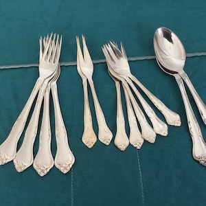 Puede incluir: Un juego de cubiertos, que incluye tenedores y una cuchara, con diseños ornamentados. Los cubiertos son de plata y tienen un acabado pulido.